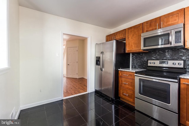 kitchen with light stone countertops, dark tile flooring, backsplash, and stainless steel appliances