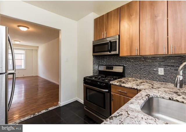 kitchen featuring light stone countertops, appliances with stainless steel finishes, backsplash, dark tile floors, and sink