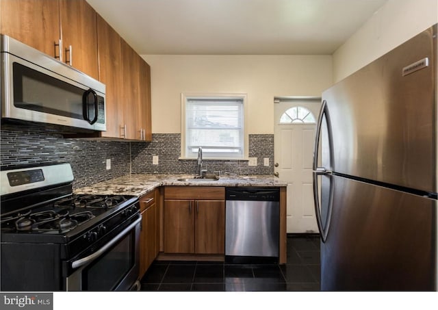 kitchen with tasteful backsplash, appliances with stainless steel finishes, dark tile flooring, light stone counters, and sink