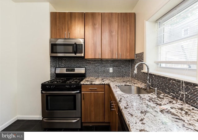 kitchen with stainless steel appliances, light stone countertops, dark tile flooring, backsplash, and sink