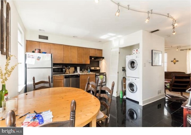 kitchen with stacked washer and dryer, dark tile flooring, and stainless steel appliances