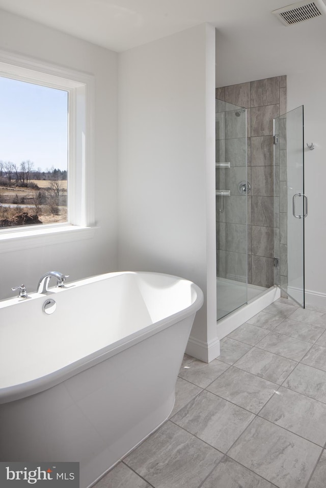 bathroom with a stall shower, visible vents, a freestanding bath, and baseboards