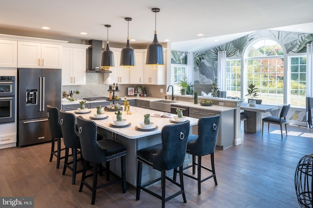 kitchen featuring wall chimney range hood, dark wood-type flooring, a kitchen island, hanging light fixtures, and stainless steel appliances