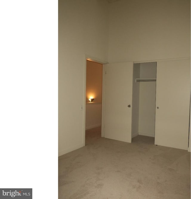 unfurnished bedroom with light carpet, a closet, and a towering ceiling