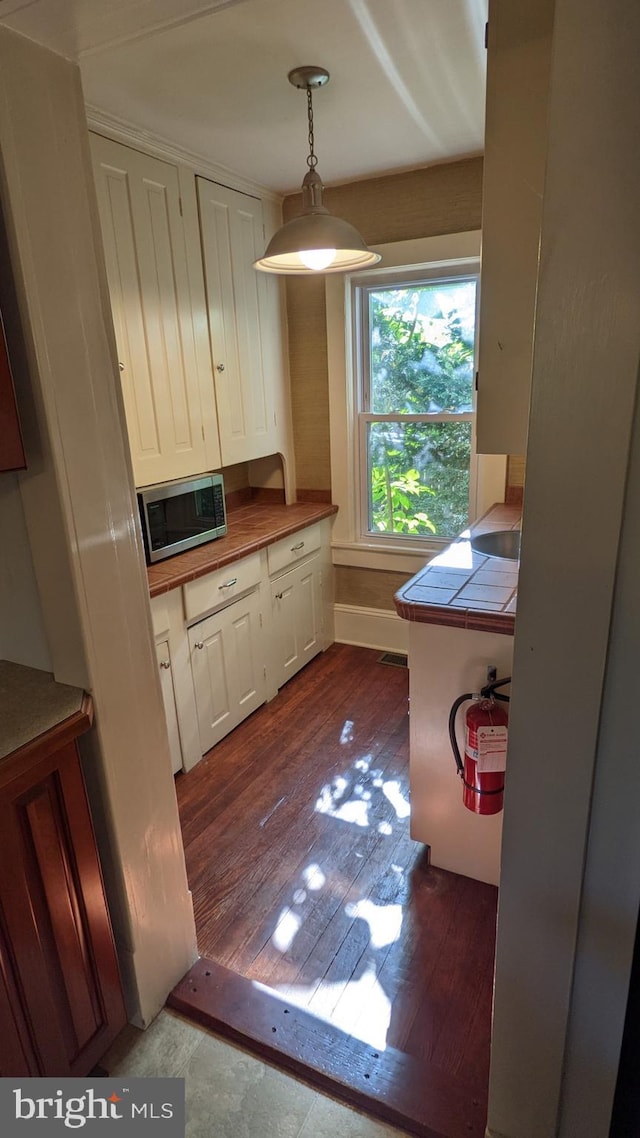 kitchen featuring white cabinets, hardwood / wood-style floors, tile counters, and pendant lighting