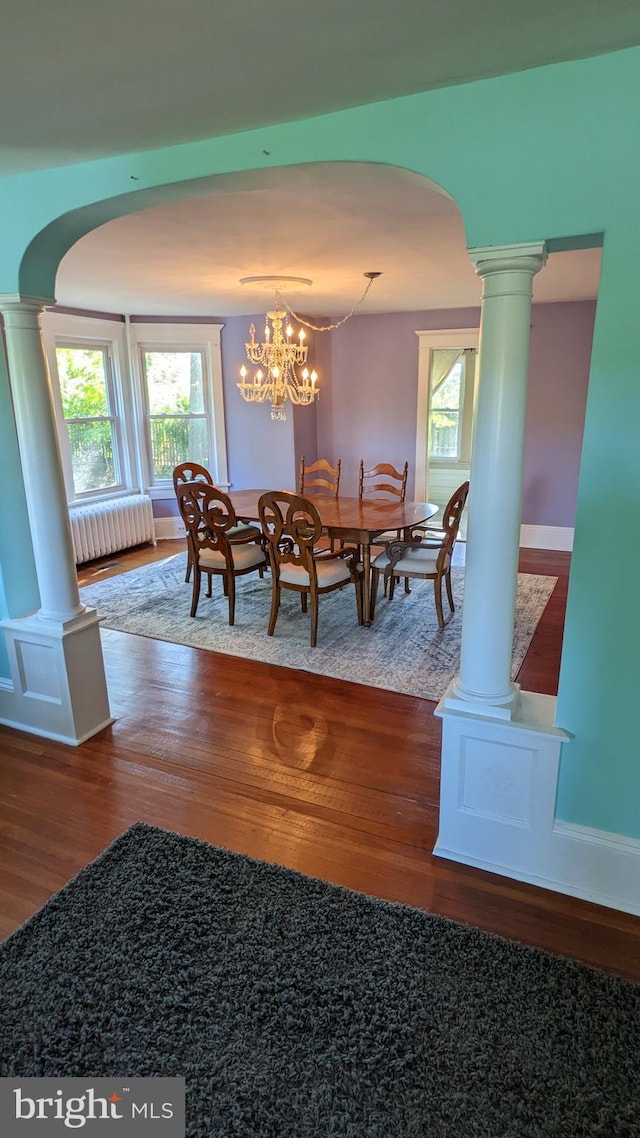 dining room with decorative columns, wood-type flooring, radiator, and a notable chandelier