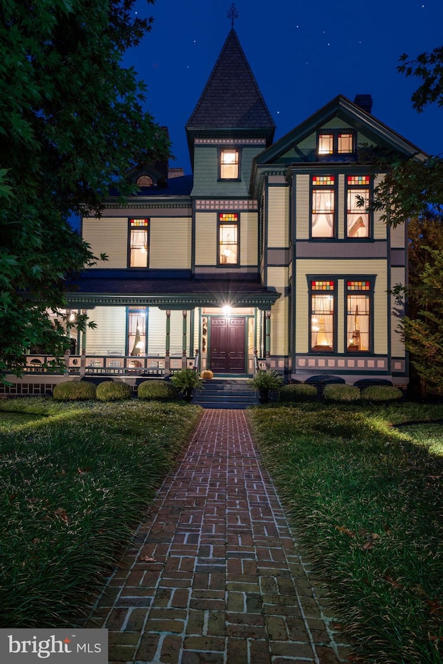 back house at night featuring a lawn and covered porch