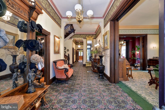 corridor with decorative columns, dark carpet, a notable chandelier, and ornamental molding