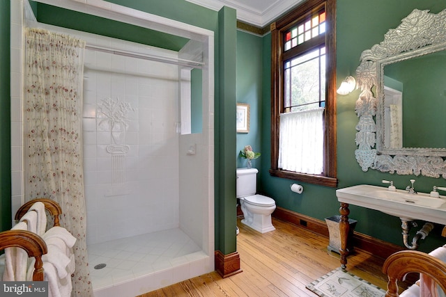 bathroom featuring toilet, wood-type flooring, a tile shower, and ornamental molding