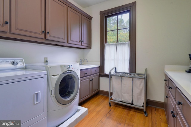 clothes washing area with cabinets, sink, washing machine and dryer, and light hardwood / wood-style flooring