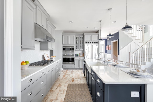 kitchen featuring gray cabinetry, built in appliances, hanging light fixtures, and light hardwood / wood-style flooring