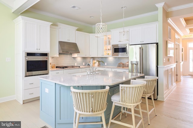 kitchen featuring white cabinetry, stainless steel appliances, a kitchen island with sink, wall chimney exhaust hood, and backsplash