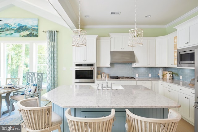 kitchen featuring wall chimney range hood, an island with sink, stainless steel appliances, and hanging light fixtures