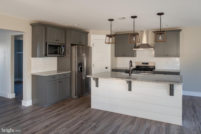 kitchen featuring gray cabinetry, a kitchen breakfast bar, hanging light fixtures, stainless steel appliances, and wall chimney range hood