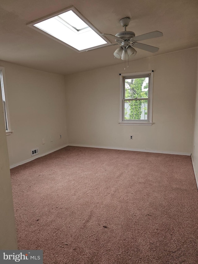 carpeted empty room featuring a skylight and ceiling fan