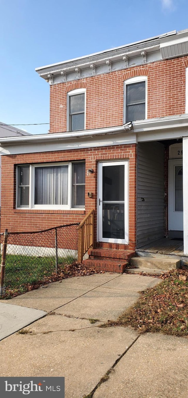 view of front of home with brick siding, entry steps, and fence