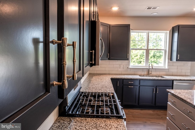 kitchen with hardwood / wood-style flooring, tasteful backsplash, stainless steel dishwasher, light stone countertops, and sink