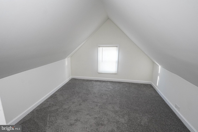 additional living space featuring vaulted ceiling and dark colored carpet