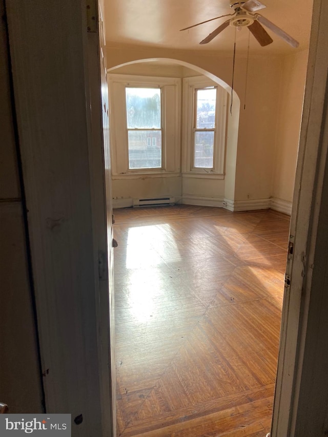 unfurnished room with ceiling fan, light parquet floors, and a baseboard heating unit