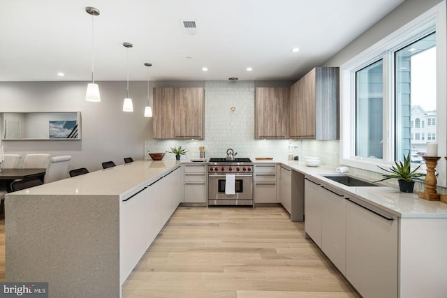 kitchen with tasteful backsplash, premium stove, light hardwood / wood-style floors, decorative light fixtures, and sink