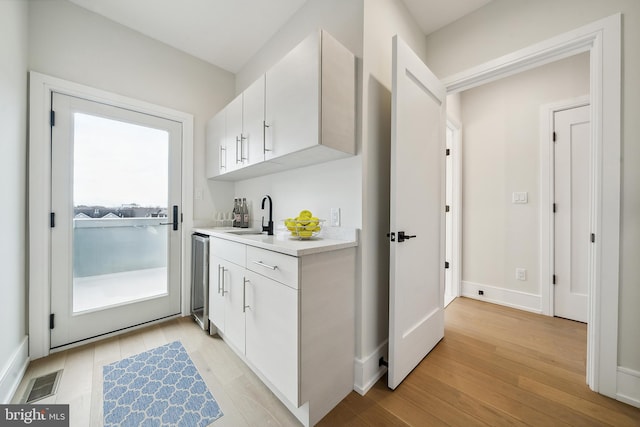 kitchen with white cabinets, wine cooler, light wood-type flooring, and sink