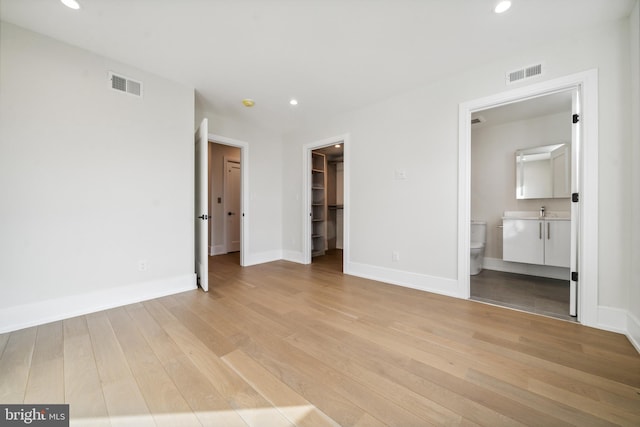 unfurnished bedroom featuring a closet, a spacious closet, ensuite bath, and light hardwood / wood-style floors