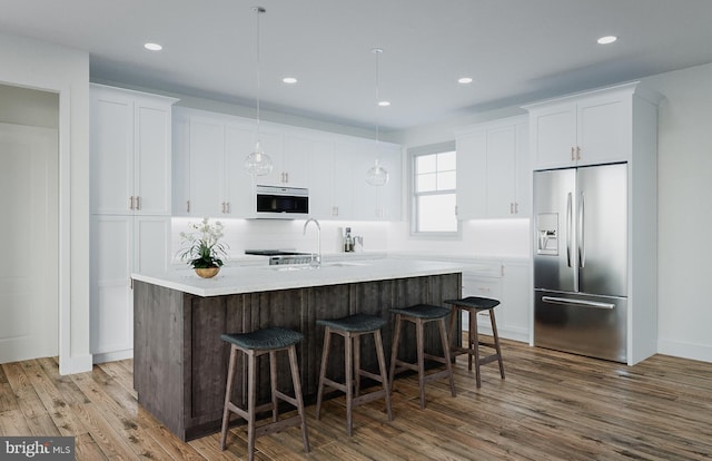 kitchen with pendant lighting, stainless steel fridge with ice dispenser, white cabinets, a center island with sink, and wood-type flooring