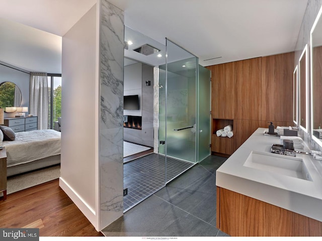 bathroom with large vanity, an enclosed shower, double sink, and wood-type flooring