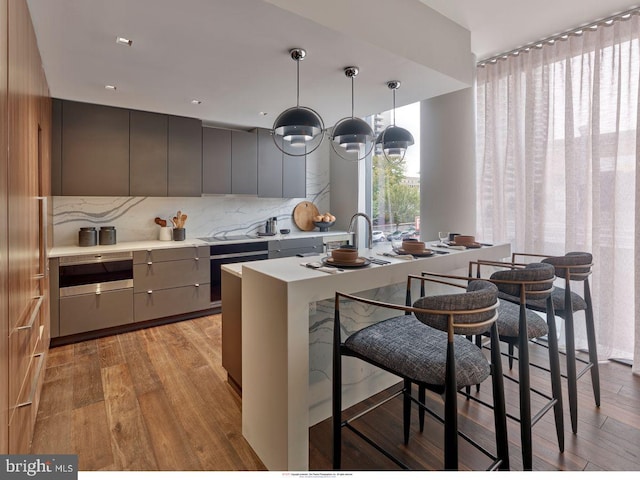 kitchen with light hardwood / wood-style floors, a kitchen bar, tasteful backsplash, gray cabinetry, and hanging light fixtures