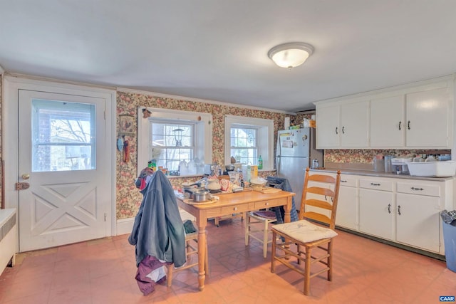 kitchen with stainless steel fridge, light tile floors, radiator, tasteful backsplash, and white cabinetry