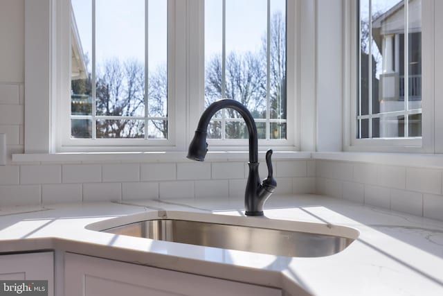 room details with light stone counters, sink, and white cabinetry