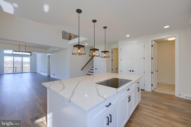 kitchen with white cabinets, a center island, decorative light fixtures, black electric stovetop, and light stone counters