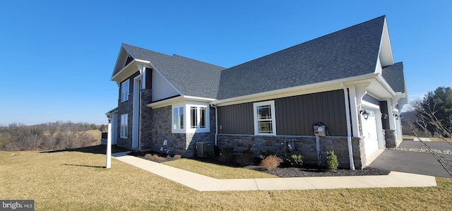 view of front of property featuring a shingled roof, central AC, a garage, stone siding, and a front lawn