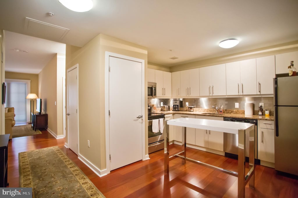 kitchen with hardwood / wood-style flooring, appliances with stainless steel finishes, tasteful backsplash, and white cabinetry