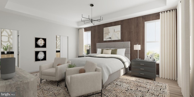 bedroom featuring an inviting chandelier, a tray ceiling, and light hardwood / wood-style floors