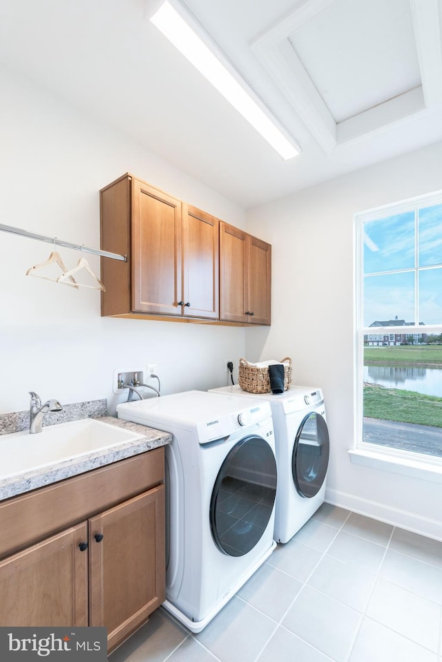 clothes washing area featuring washing machine and clothes dryer, sink, a water view, cabinets, and light tile patterned floors