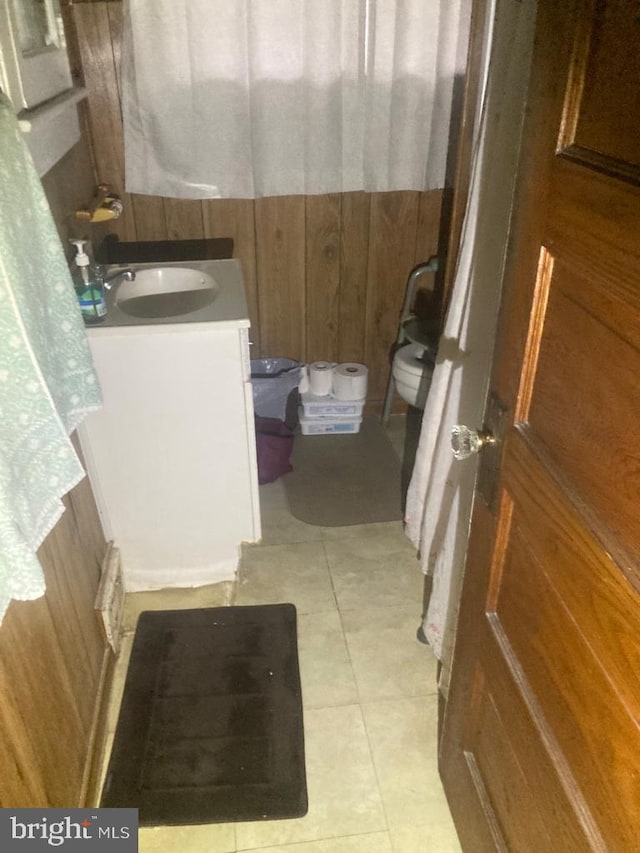 bathroom with wooden walls, vanity, tile flooring, and toilet