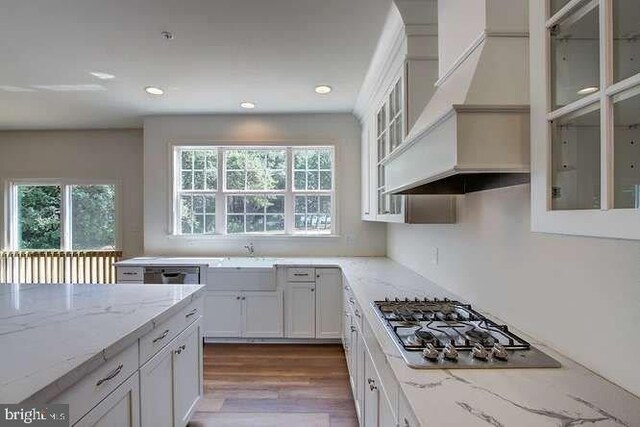 kitchen featuring custom range hood, wood finished floors, stainless steel gas stovetop, white cabinets, and light stone countertops