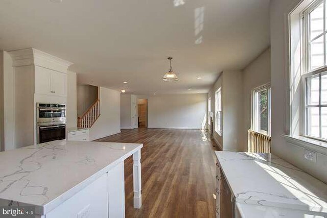 kitchen with light stone counters, wood finished floors, white cabinets, pendant lighting, and double oven