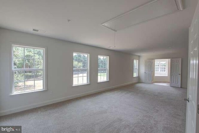 carpeted spare room with a healthy amount of sunlight, attic access, and baseboards