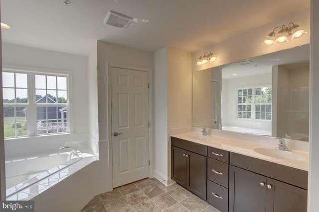 bathroom featuring double vanity, a garden tub, a wealth of natural light, and a sink