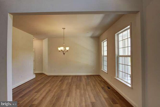 unfurnished dining area featuring baseboards, a notable chandelier, and wood finished floors