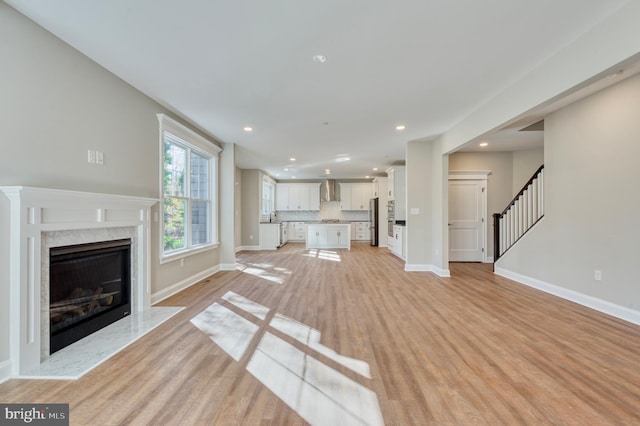 unfurnished living room featuring baseboards, a premium fireplace, recessed lighting, stairs, and light wood-type flooring