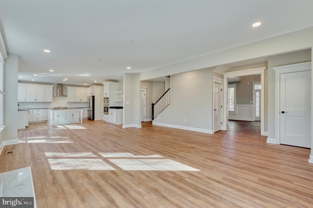 unfurnished living room featuring recessed lighting, stairway, light wood-style flooring, and baseboards