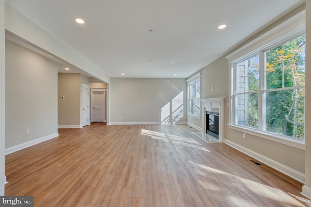 unfurnished living room with visible vents, recessed lighting, light wood finished floors, a premium fireplace, and baseboards