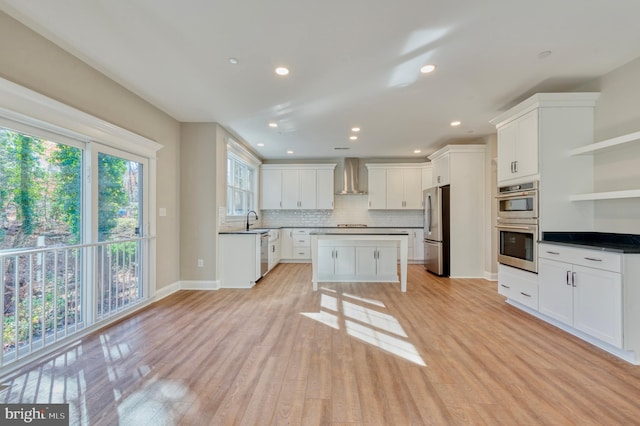 kitchen featuring open shelves, light wood-style flooring, appliances with stainless steel finishes, wall chimney range hood, and backsplash