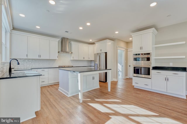 kitchen featuring light wood finished floors, appliances with stainless steel finishes, wall chimney exhaust hood, and open shelves