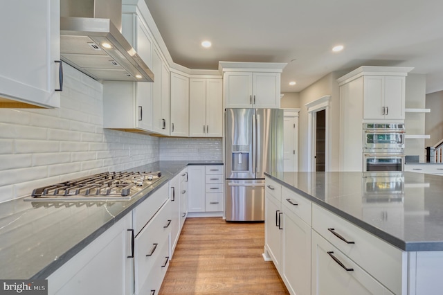 kitchen with tasteful backsplash, light wood-type flooring, white cabinets, stainless steel appliances, and wall chimney exhaust hood