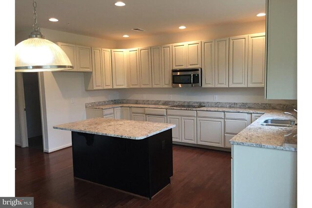 kitchen featuring light stone counters, stainless steel microwave, black electric cooktop, and a sink