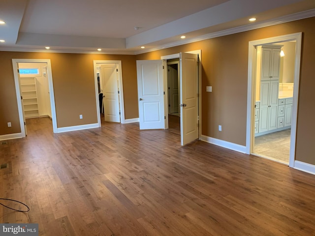 unfurnished bedroom with connected bathroom, a spacious closet, a tray ceiling, and dark wood-type flooring